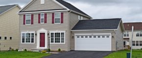 Exterior of house with tan siding, red front door, white garage door and trim, driveway, and lawn