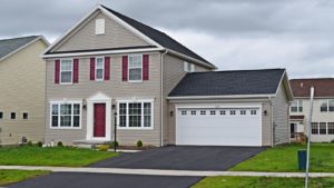 Exterior of house with tan siding, red front door, white garage door and trim, driveway, and lawn