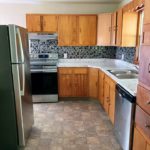 Kitchen with light wood cabinets, stainless steel and white appliances, and tile backsplash