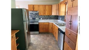 Kitchen with light wood cabinets, stainless steel and white appliances, and tile backsplash