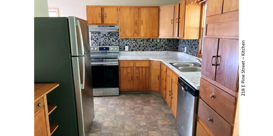 Kitchen with light wood cabinets, stainless steel and white appliances, and tile backsplash