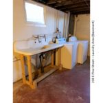 Unfinished basement with large wash tub, and side-by-side washer and dryer
