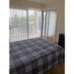 Carpeted bedroom with large bed, chest of drawers, and sliding door onto balcony
