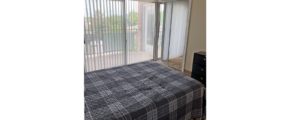 Carpeted bedroom with large bed, chest of drawers, and sliding door onto balcony