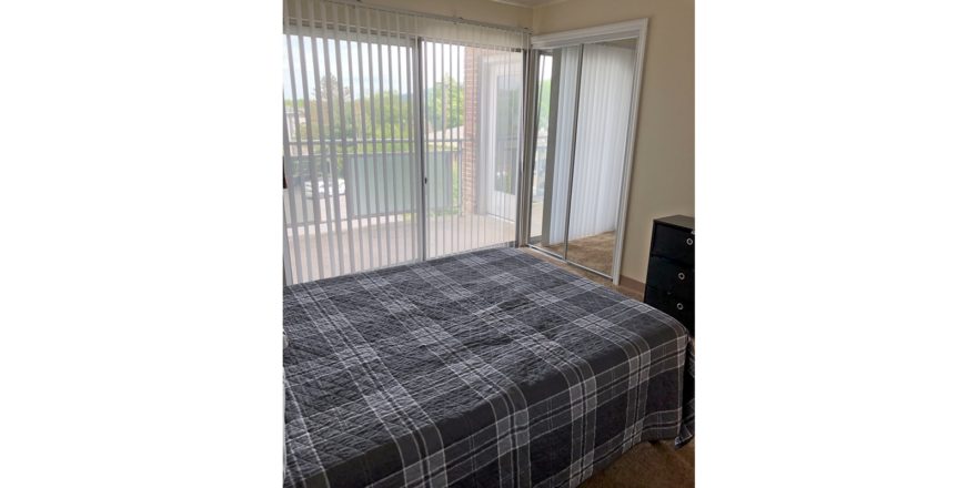 Carpeted bedroom with large bed, chest of drawers, and sliding door onto balcony