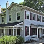 Exterior of duplex with covered front and side porches, light siding, and maroon shutters.