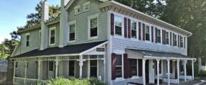 Exterior of duplex with covered front and side porches, light siding, and maroon shutters.