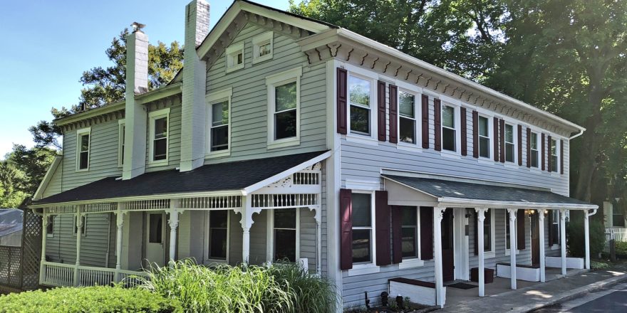 Exterior of duplex with covered front and side porches, light siding, and maroon shutters.