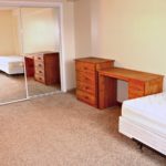 Bedroom with two twin beds, wooden desk, and wooden chest of drawers