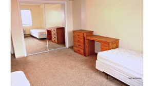 Bedroom with two twin beds, wooden desk, and wooden chest of drawers