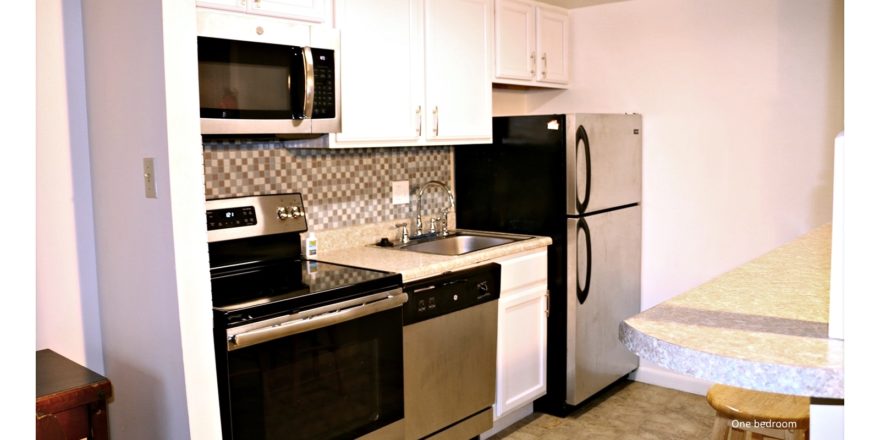 Kitchen with white cabinets, stainless steel appliances, barstool seating, and backsplash