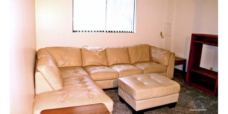 Living room with large sectional sofa, ottoman, accent tables, and TV stand