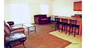 Open concept living room/kitchen with island with barstool seating, couches, and accent table