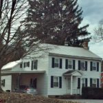 Exterior of two story house with carport. It has white siding, black shutters and a covered entry