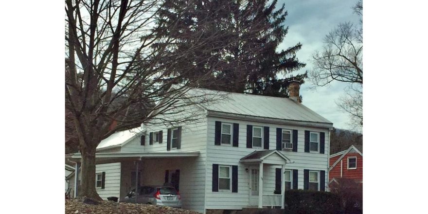 Exterior of two story house with carport. It has white siding, black shutters and a covered entry