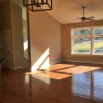 Living room with vaulted ceilings, hardwood floors, large picture window, and ceiling fan