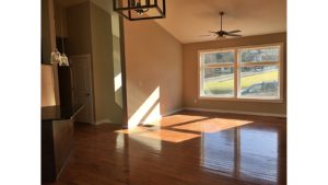 Living room with vaulted ceilings, hardwood floors, large picture window, and ceiling fan