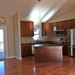 Open kitchen with island, stainless steel appliances, tile backsplash, pendant lighting, cherry wood cabinets and stone countertops