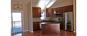 Open kitchen with island, stainless steel appliances, tile backsplash, pendant lighting, cherry wood cabinets and stone countertops