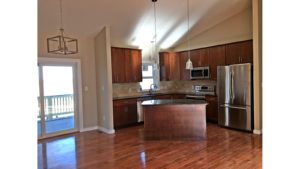 Open kitchen with island, stainless steel appliances, tile backsplash, pendant lighting, cherry wood cabinets and stone countertops