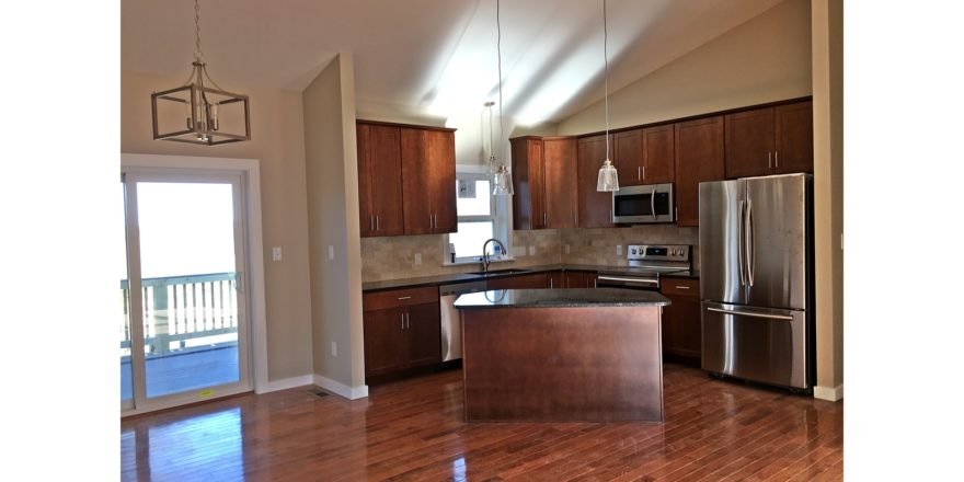 Open kitchen with island, stainless steel appliances, tile backsplash, pendant lighting, cherry wood cabinets and stone countertops