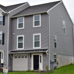 Exterior of townhouse with gray siding, black front door, with a one car garage and driveway