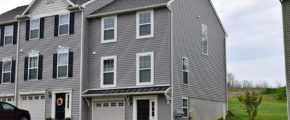 Exterior of townhouse with gray siding, black front door, with a one car garage and driveway