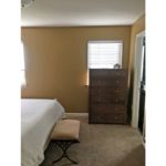 Bedroom with two windows, wooden dresser with seven drawers, stool, and queen bed