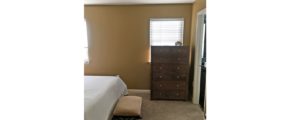 Bedroom with two windows, wooden dresser with seven drawers, stool, and queen bed