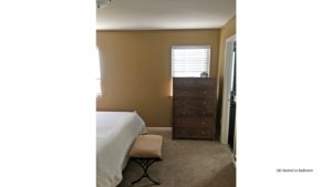 Bedroom with two windows, wooden dresser with seven drawers, stool, and queen bed