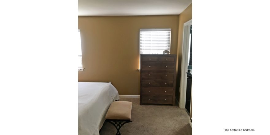 Bedroom with two windows, wooden dresser with seven drawers, stool, and queen bed