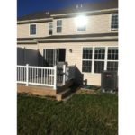 Exterior of townhouse with light tan siding and deck with sliding glass door.