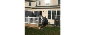Exterior of townhouse with light tan siding and deck with sliding glass door.