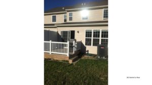 Exterior of townhouse with light tan siding and deck with sliding glass door.