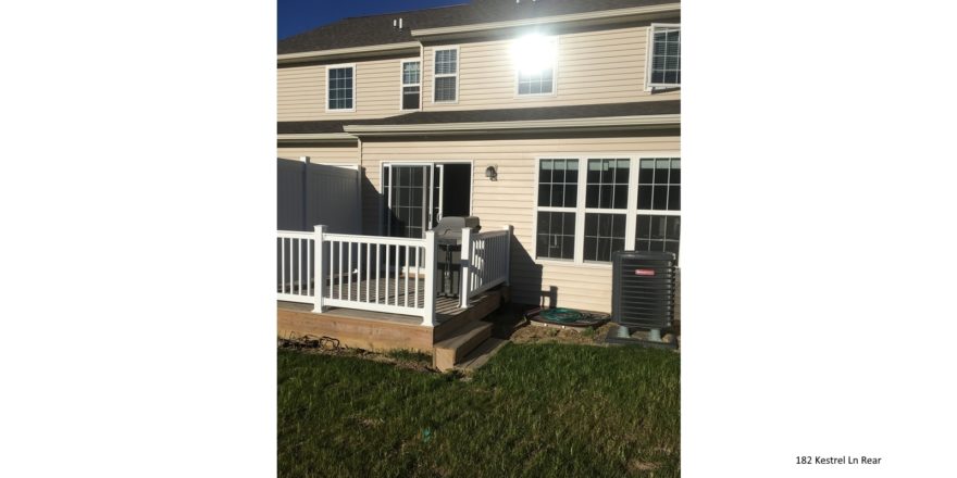 Exterior of townhouse with light tan siding and deck with sliding glass door.