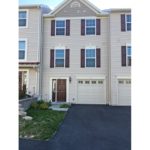 Exterior of townhouse with light tan siding and maroon front door and shutters