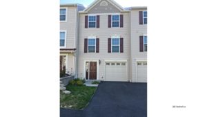 Exterior of townhouse with light tan siding and maroon front door and shutters