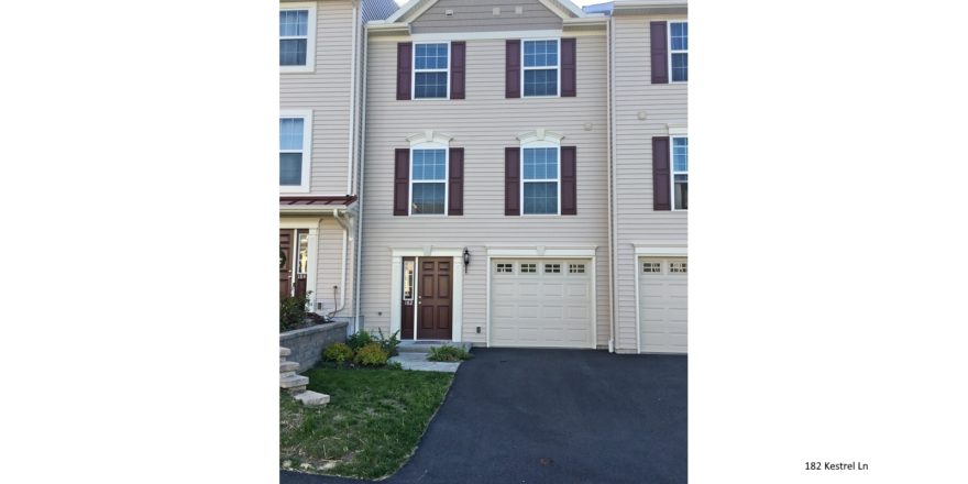 Exterior of townhouse with light tan siding and maroon front door and shutters