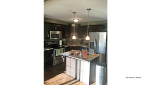 Kitchen with wood-style floor, stainless steel appliances, dark wood cabinets, and island