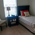 Carpeted bedroom with twin bed, nighstand, chair and mirror