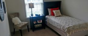 Carpeted bedroom with twin bed, nighstand, chair and mirror