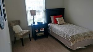 Carpeted bedroom with twin bed, nighstand, chair and mirror