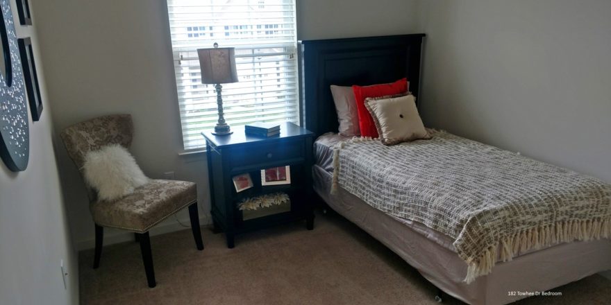 Carpeted bedroom with twin bed, nighstand, chair and mirror