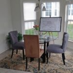Dining room with tile flooring, accent rug, glass table with chairs, and large bay window