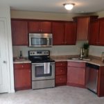 Kitchen with stainless steel appliances, tile floor, cherry wood cabinets and marble-style countertops