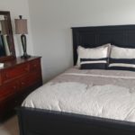 Carpeted bedroom with queen bed, wood dresser with seven drawers, mirror, and nightstand