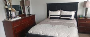 Carpeted bedroom with queen bed, wood dresser with seven drawers, mirror, and nightstand