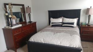 Carpeted bedroom with queen bed, wood dresser with seven drawers, mirror, and nightstand