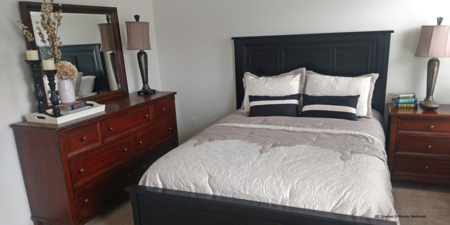 Carpeted bedroom with queen bed, wood dresser with seven drawers, mirror, and nightstand