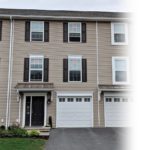Exterior of townhouse with tan siding and dark brown shutters and front door
